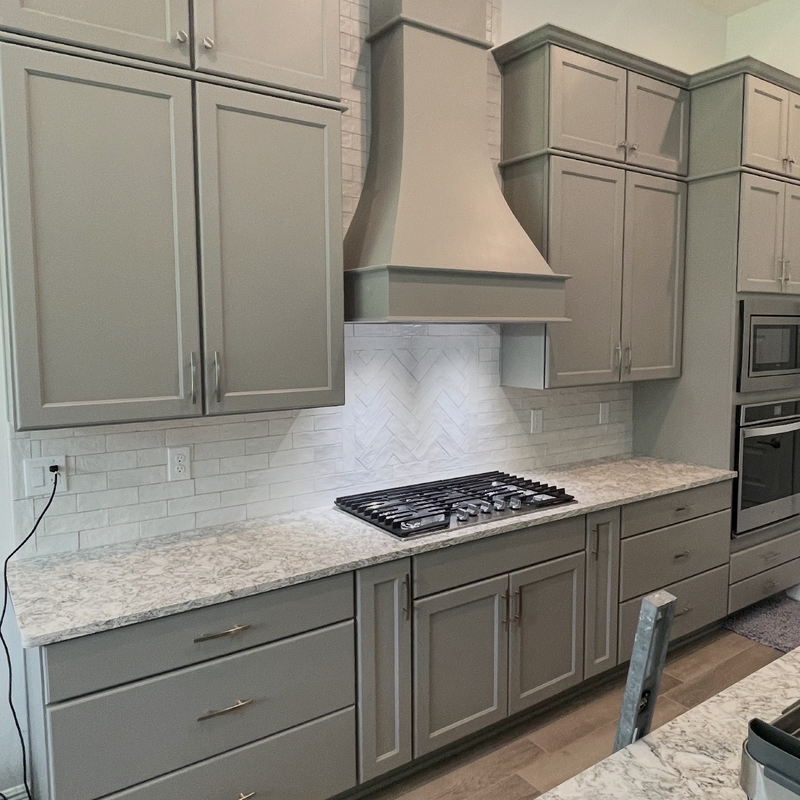 Kitchen remodel with gray cabinets, a range hood and herringbone tile backsplash